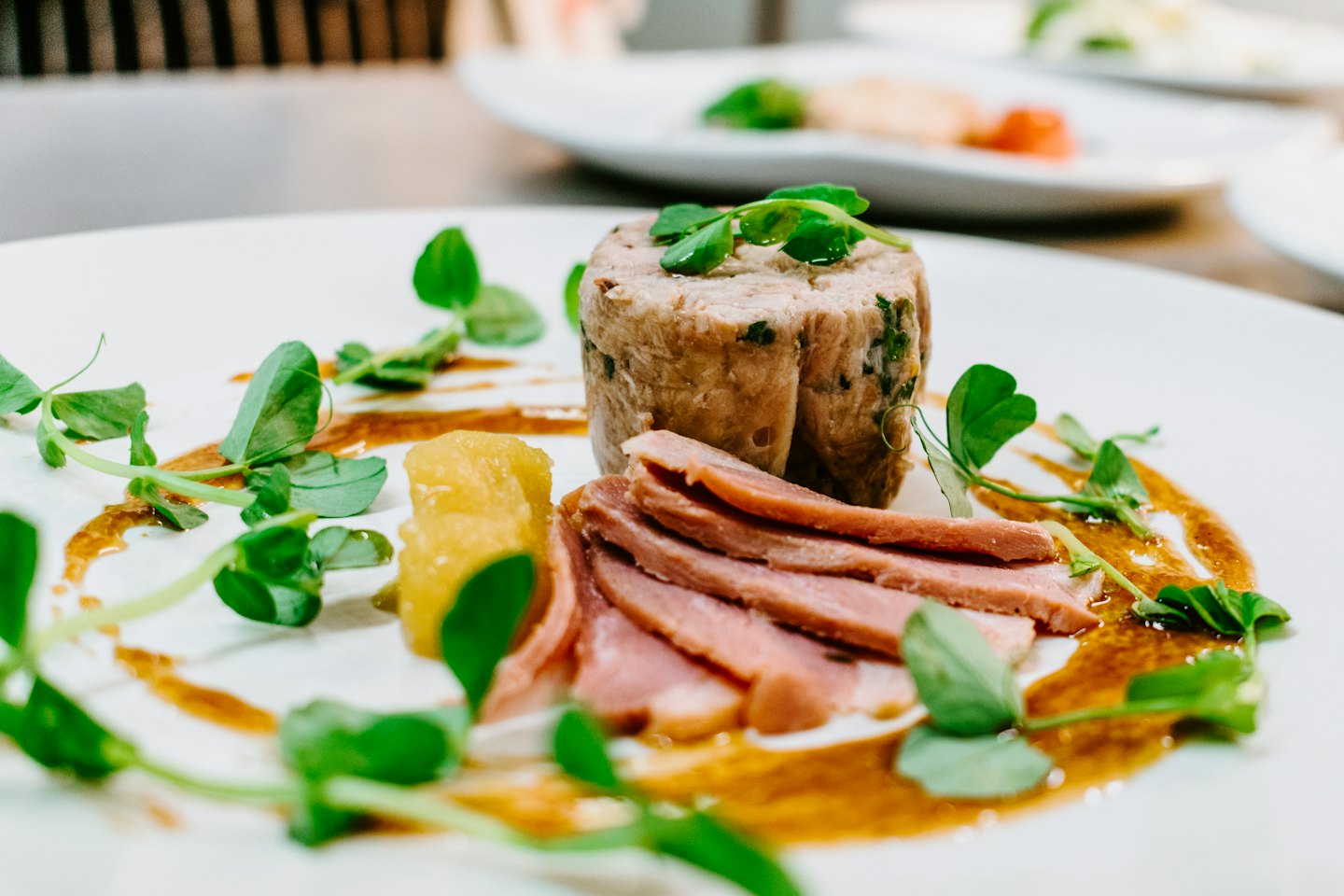 Gourmet-Fleischgericht mit gelbem Relish und Microgreens auf weißem Teller.