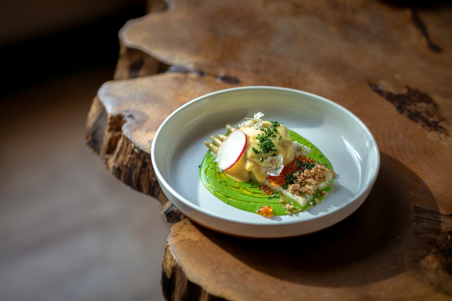 Gourmet-Gericht mit bunter Sauce, Rogen und Blumen auf einem Holztisch.